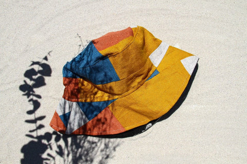 Not I But We's Mustard Blue Bucket Hat made with linen offcuts in different shades of mustard, orange, and blue.