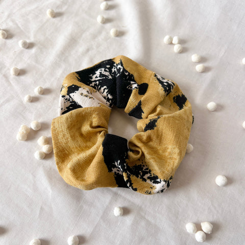 Yellow scrunchie with black and white pattern on a light gray background