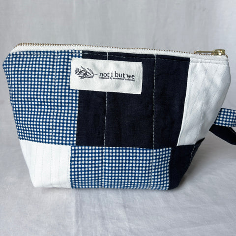 Patchwork pouch with blue and white checkered pattern and 'not i but we' label