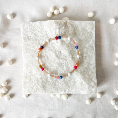 Colorful beaded bracelet on a white textured surface with scattered beads.