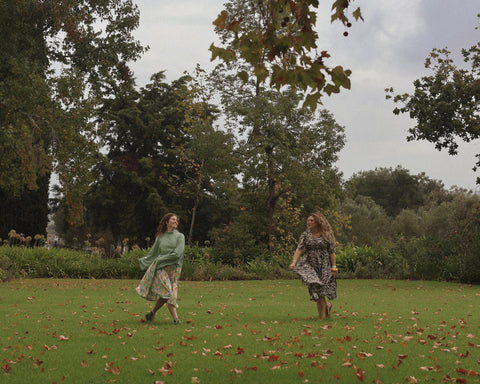 two women wearing not i but we sisterhood dress in a field