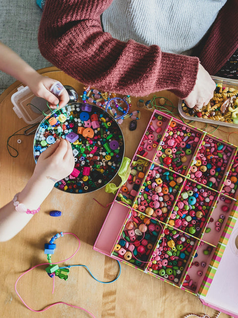 two people sitting at a table using colourful beads