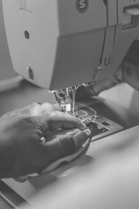 Close-up of a sewing machine with a hand operating it, in black and white.