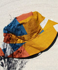 Not I But We's Mustard Blue Bucket Hat made with linen offcuts in different shades of mustard, orange, and blue.