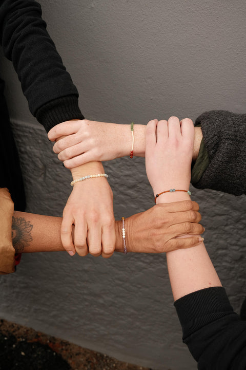 Not I But We's Mindful bracelets worn by different women holding each others wrists.