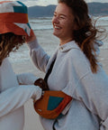 Two young women smiling while wearing the patchwork bucket hats and moonbag.