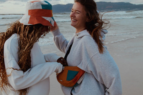 Two young women smiling while wearing the patchwork bucket hats and moonbag.