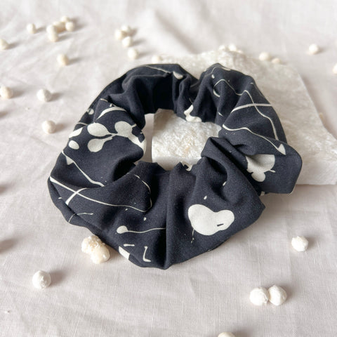 Black scrunchie with white patterns on a light fabric background