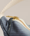 Close-up of a blue textured fabric with a gold zipper on a light gray background
