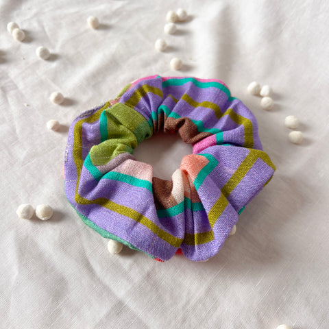 Multicolored striped scrunchie on a textured white surface with scattered beads.