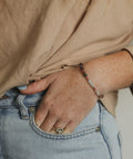 A close-up lifestyle shot of a person wearing a delicate beaded bracelet on their wrist, paired with a beige top and light blue jeans.