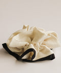 White fabric item with black trim on a light beige background