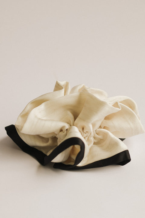 White fabric item with black trim on a light beige background