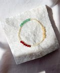 Bracelet with green and red beads on a white stone surface