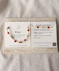 Bracelet with red beads on a card with text and QR code, on a light fabric background