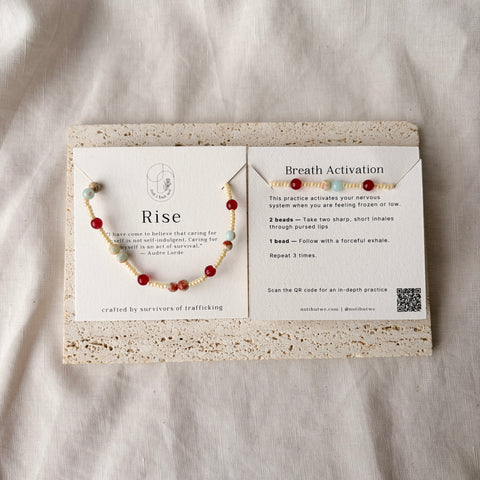 Bracelet with red beads on a card with text and QR code, on a light fabric background