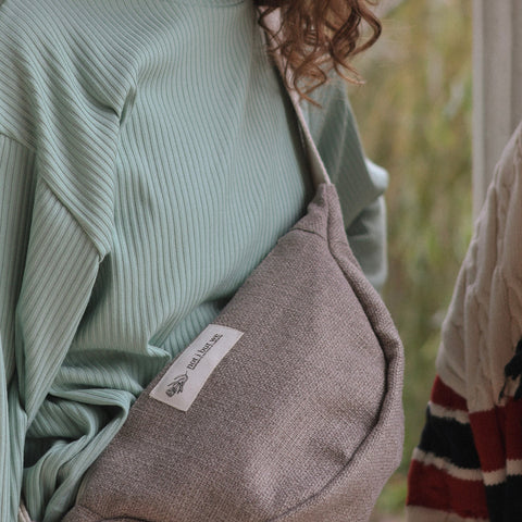 Person wearing a light green ribbed sweater with a gray bag featuring a logo.